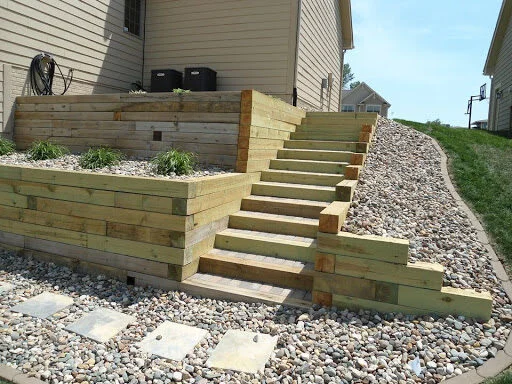 Tiered wooden timber retaining wall with built-in wooden staircase and gravel rock beds