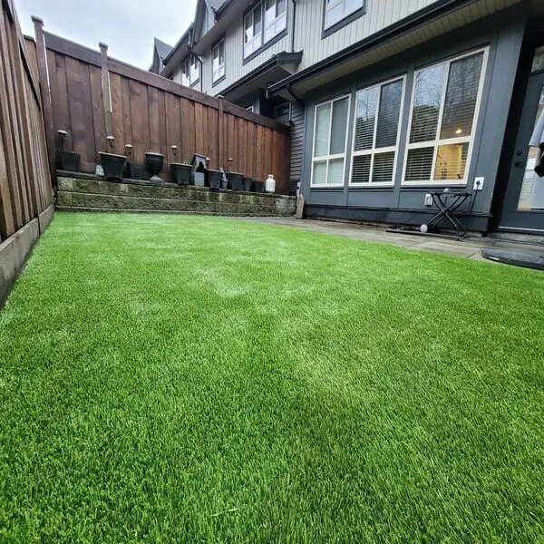 Artificial turf lawn in a small residential backyard with a wooden fence and house