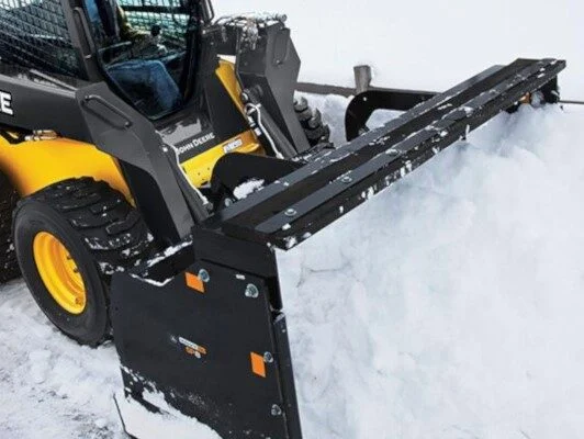 Heavy machinery skid steer loader pushing and clearing thick winter snow with a front plow blade